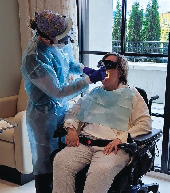 A dental hygienist providing care to a resident seated in her wheelchair beside a bright window